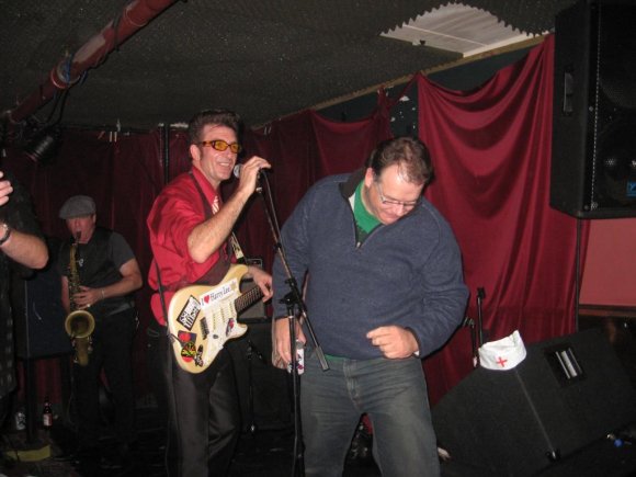 GREG (RUBBER ROOM RATS) delivers a beer to LUIGI BABE on stage.