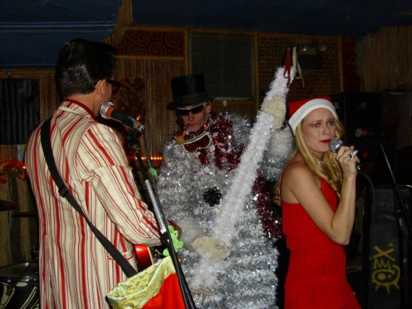 LUIGI BABE watches as FATHER RICHIE CHRISTMAS skate-dances around HILLARY.