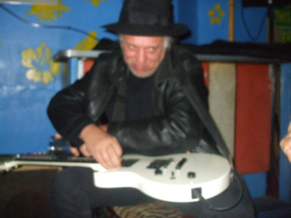 JOE decides he might as well wear JOFF's hat as he plays the left-handed guitar, cross-armed!