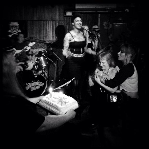 CYNDI holds PHYLISS back as COLLEEN holds the cake and MIKE, CYD, LAUREN and KENN sing 'HAPPY BIRTHDAY!"