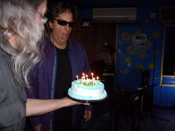 ARMAND holds the cake as CHARLES gets ready to blow out the candles!